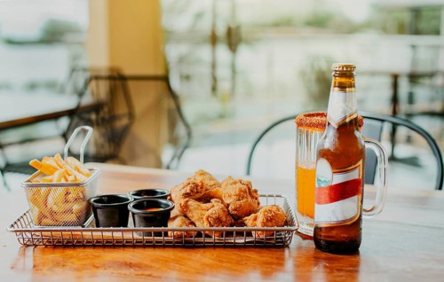 Traditional spicy chicken wings with fries and michelada accompanied with beer served on wooden