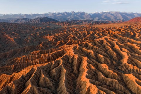Landscape of eroded hills, badlands at sunset, mountain peaks of the Tian Shan Mountains in the