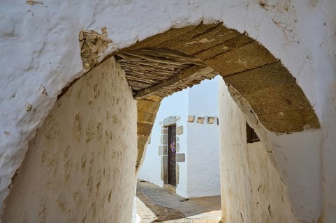 Narrow arched passageway with white walls and wooden beams in a quiet alley, Chora, Old Town,