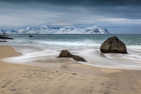 Rocks on the beach in front of snowy mountains, dark clouds, sea, spray, winter, Vikten,