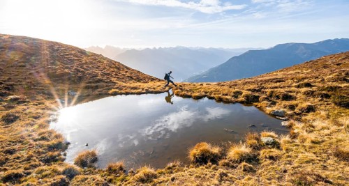 Mountaineer jumping, reflected in a small mountain lake on the Krahberg, mountain panorama in
