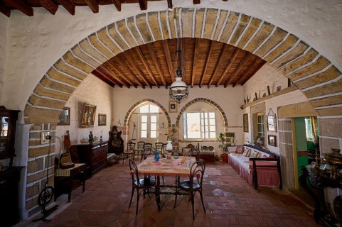 Dining room with round arch, rustic wooden floors and antique furniture. Bright windows let in