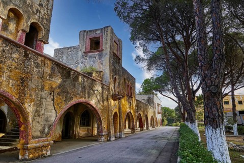 A long corridor of a historic, dilapidated building with arches and trees along the street, Italian