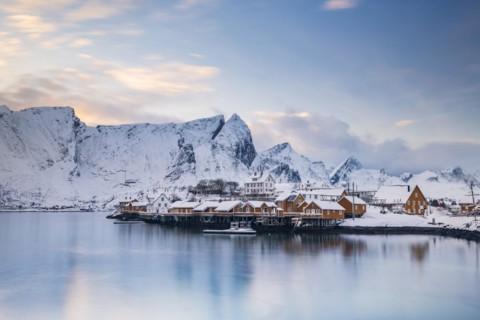 Traditional yellow rorbuer huts on the island of Sakrisoy, snow-capped mountains in the background,