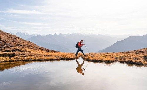 Mountaineer hiking with poles, reflected in a small mountain lake on the Krahberg, mountain