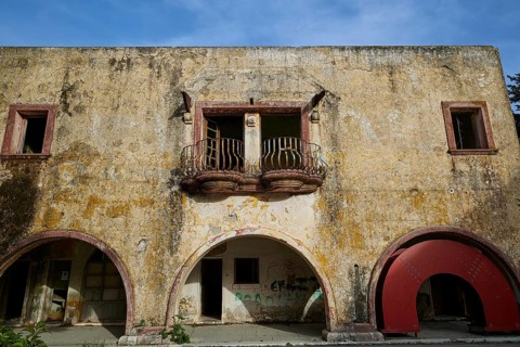 The dilapidated façade of a historic building with a yellow wall, several windows and decorative