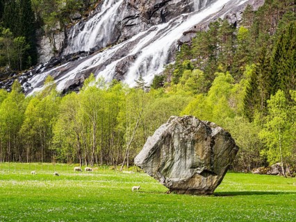 Single large rock Oddmundsteinen on farmland, waterfall in the back, greasing sheep, spring, south