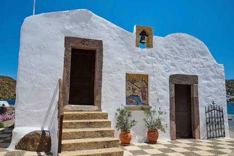 White building in traditional Greek style with staircase, two doors and bell, under blue sky and in