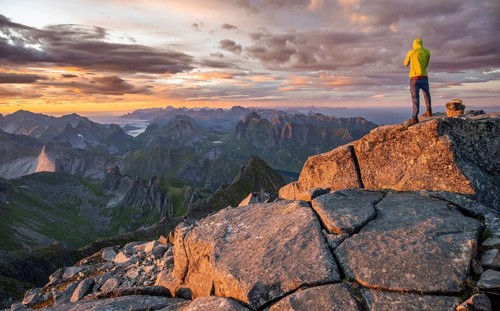 View over mountain top and sea, dramatic sunset, climbers at the top of Hermannsdalstinden,