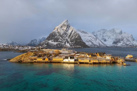 Traditional yellow rorbuer cabins on Sakrisoy Island, snow-capped rocky mountains in the back,
