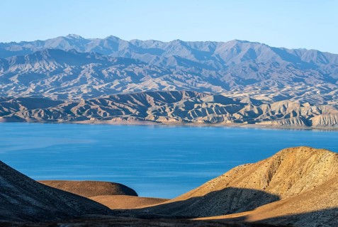 Blue Toktogul reservoir between dry mountain landscape, hilly mountains in the evening light,