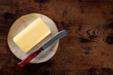 A block of butter with a knife on a plate, shot from above a dark rustic wooden background with