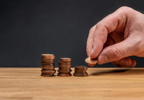 A hand stacking coins on a wooden table against a dark background