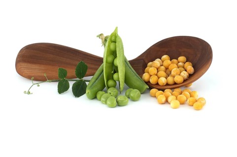 Wooden spoon filled with a yellow dried peas surrounded by a green leaf, fresh green peas and pea