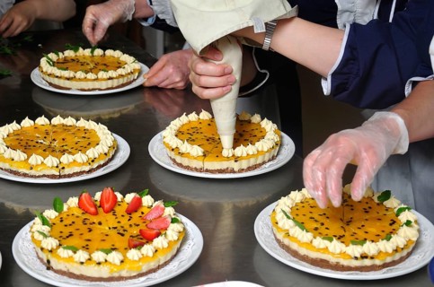 Cook placing cream on the top of a passionfruit cheesecake