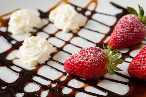 Close up of strawberries and whipped cream with decorations over a white plate