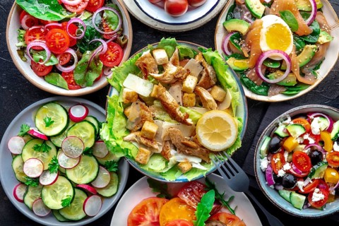 Fresh salads, overhead flat lay shot of an assortment. Variety of plates and bowls with green