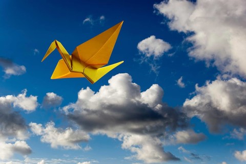 Yellow origami paper aeroplane in the sky