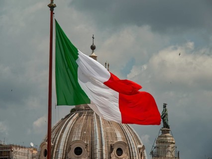 The Italian flag flies in front of a dome and a sculpture under a cloudy sky, rome, italy