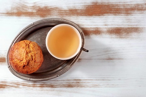 Orange muffin with tea on a rustic wooden kitchen table, on a vintage tray, overhead flat lay shot