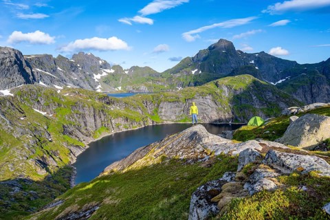 Mountaineer standing on a rock with green camping tent, mountain landscape with lake Tennesvatnet,