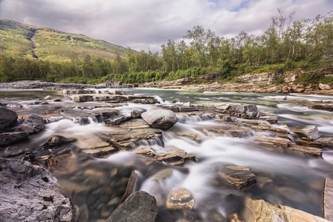 Abiskojakka, river in Abisko NP (northern Sweden) . Long exposure, rocks, birch, clouds, grey sky,