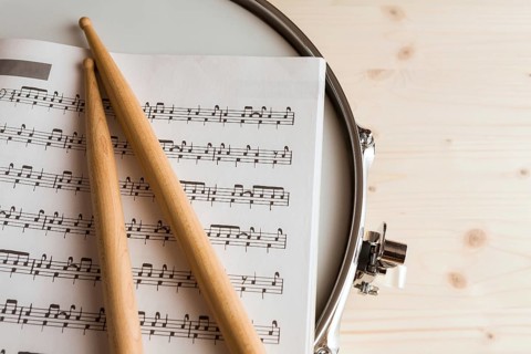 Music score and drumsticks over a snare drum with wood background