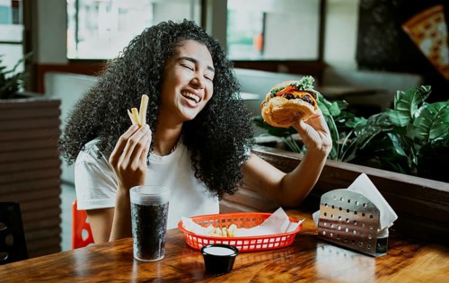 Happy girl enjoying a hamburger in a restaurant. Afro young woman enjoying a hamburger with fries