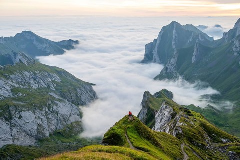 Two hikers enjoying the view over the Säntis mountains into the valley of Meglisalp at sunrise,
