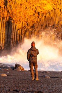 A tourist man on the black sand beach of Reynisfjara at sunset in Iceland