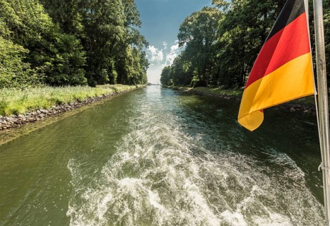 Drive shaft of a boat passing through a canal with a waving German flag