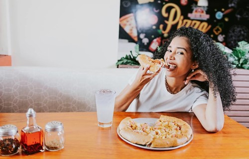 Smiling young woman enjoying a pizza in a restaurant. Happy afro hair girl eating pizza in a