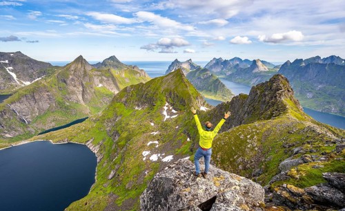 Mountaineer stretching his arms in the air, at the summit of Munken, mountain landscape with steep