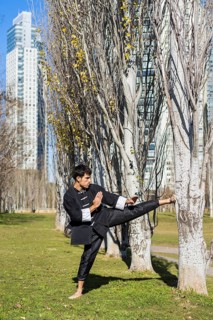 An athletic martial arts fighter practicing kicks in a public park.