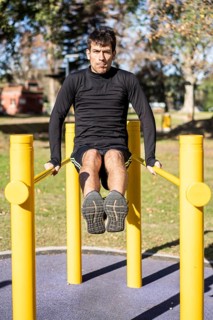 Frotn view of a young man doing abdominal exercises on a public equipment in outdoor fitness
