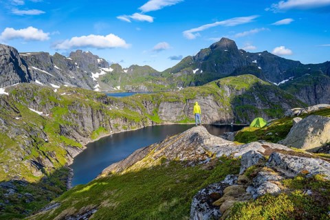 Mountaineer standing on a rock with green camping tent, mountain landscape with lake Tennesvatnet,