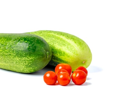 Field cucumbers (Cucumis sativus) and cocktail tomatoes (Solanum lycopersicum), on white, copy room
