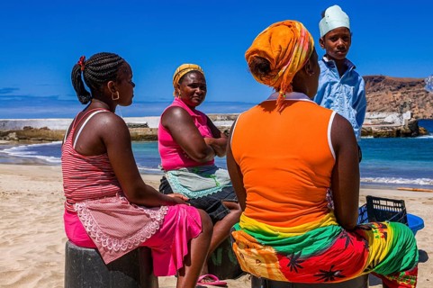 Dark skinned women, sitting at sandbeach and talking to each other. Tarrafal. Santiago. Cabo Verde.