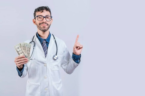 Handsome smiling doctor showing money and pointing side. Happy young doctor holding money and