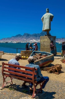 People sitting on bench in front of sculpture. San Vincente. Mindelo. Cabo Verde. Africa