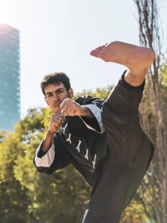 Handsome martial arts fighter practicing kicks outdoors while looking at camera