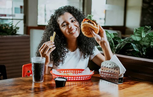 Afro young woman enjoying a hamburger with fries in a restaurant. Happy girl enjoying a hamburger