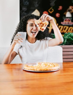 Happy afro hair woman showing slice of pizza in a restaurant. Smiling afro woman enjoying a pizza