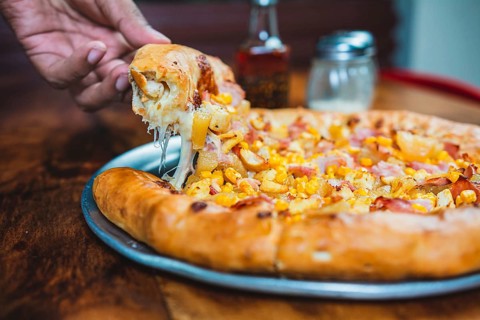 Hand taking a slice of ham and sweetcorn pizza. Homemade ham pizza with cheese and sweet corn