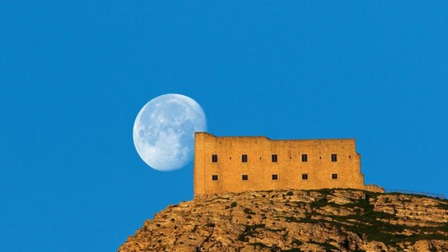 Morning light, super clear blue sky, huge full moon, fortress-like building on the mountain,