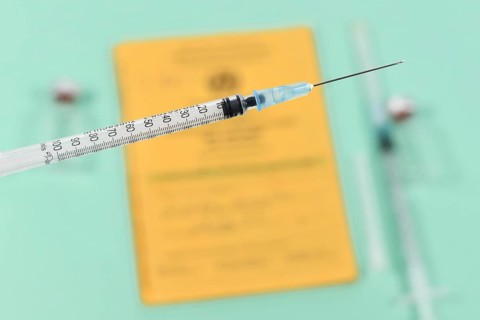 Vaccine concept with close up of syringe in front of blurry yellow international certificate of