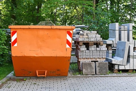 Orange industrial transportable dumpster container and cobble stones on palette at construction