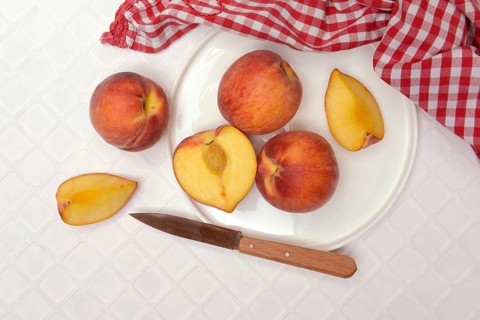 Cut peaches with knife on plate (Prunus persica)