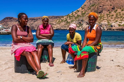 Dark skinned women, sitting at sandbeach and talking to each other. Tarrafal. Santiago. Cabo Verde.