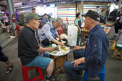 Old men sitting on plastic stools and eating at Gwangjang Market, traditional street market in